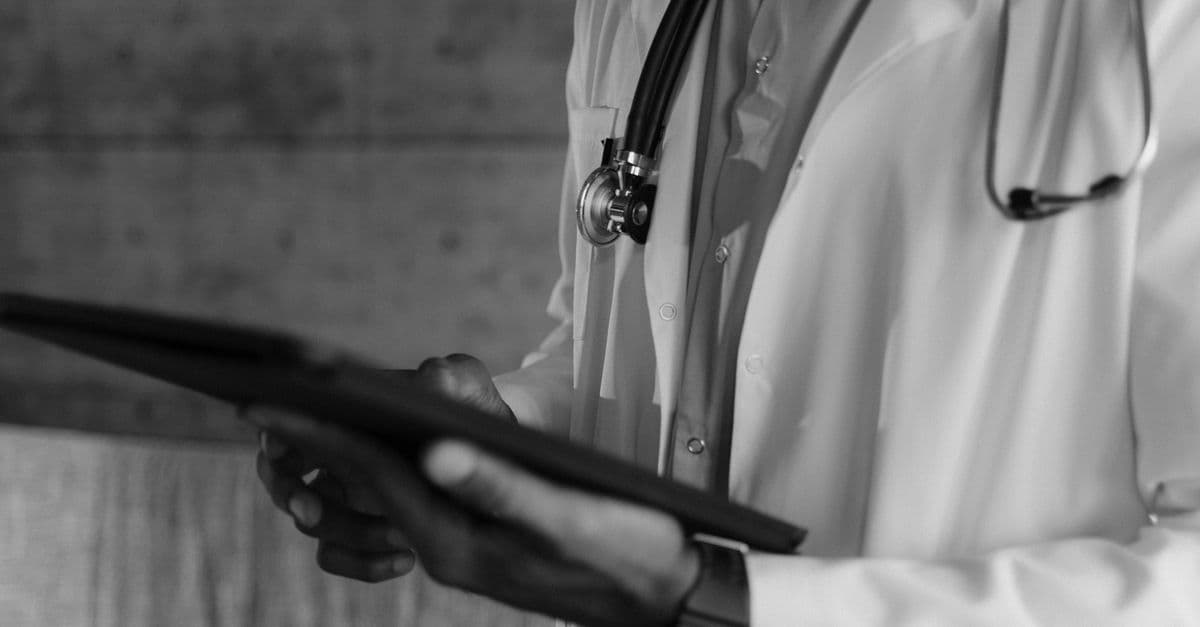 Black-and-white photo of a medical professional holding a tablet, focusing on digital health technology.