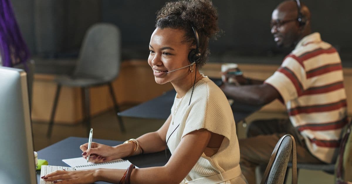 Cheerful woman in a call center using a headset and computer while working.