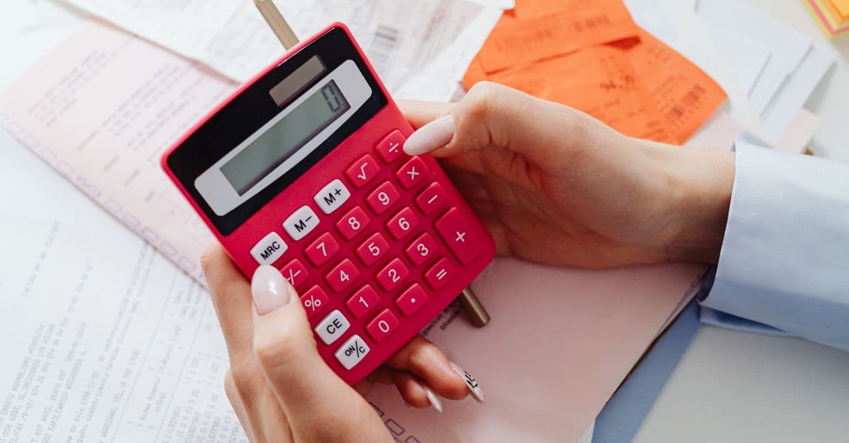 Close-up of hands holding a red calculator, managing finances with documents and receipts.
