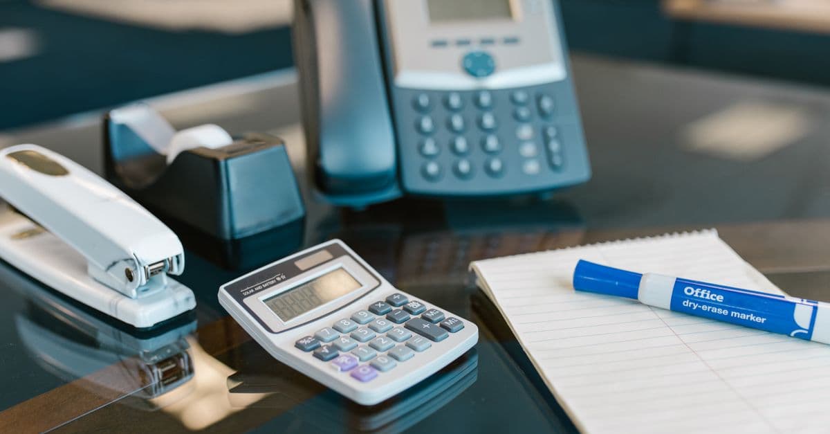 A modern office desk setup featuring various essential supplies including a calculator, stapler, and telephone.