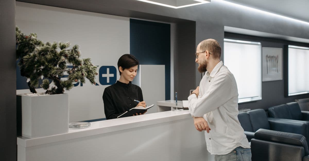 A man consults a receptionist in a modern clinic setting with contemporary design.